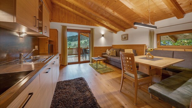 Eine moderne Küche mit Holzschränken, ein Essbereich mit Tisch und Bänken sowie ein Blick auf einen Balkon.