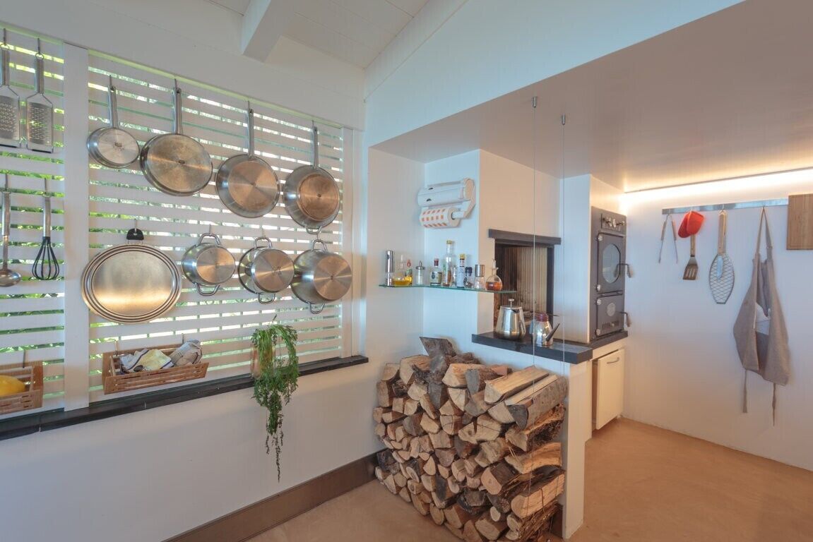 A modern kitchen with hanging pots, a coffee machine, and a stack of firewood.