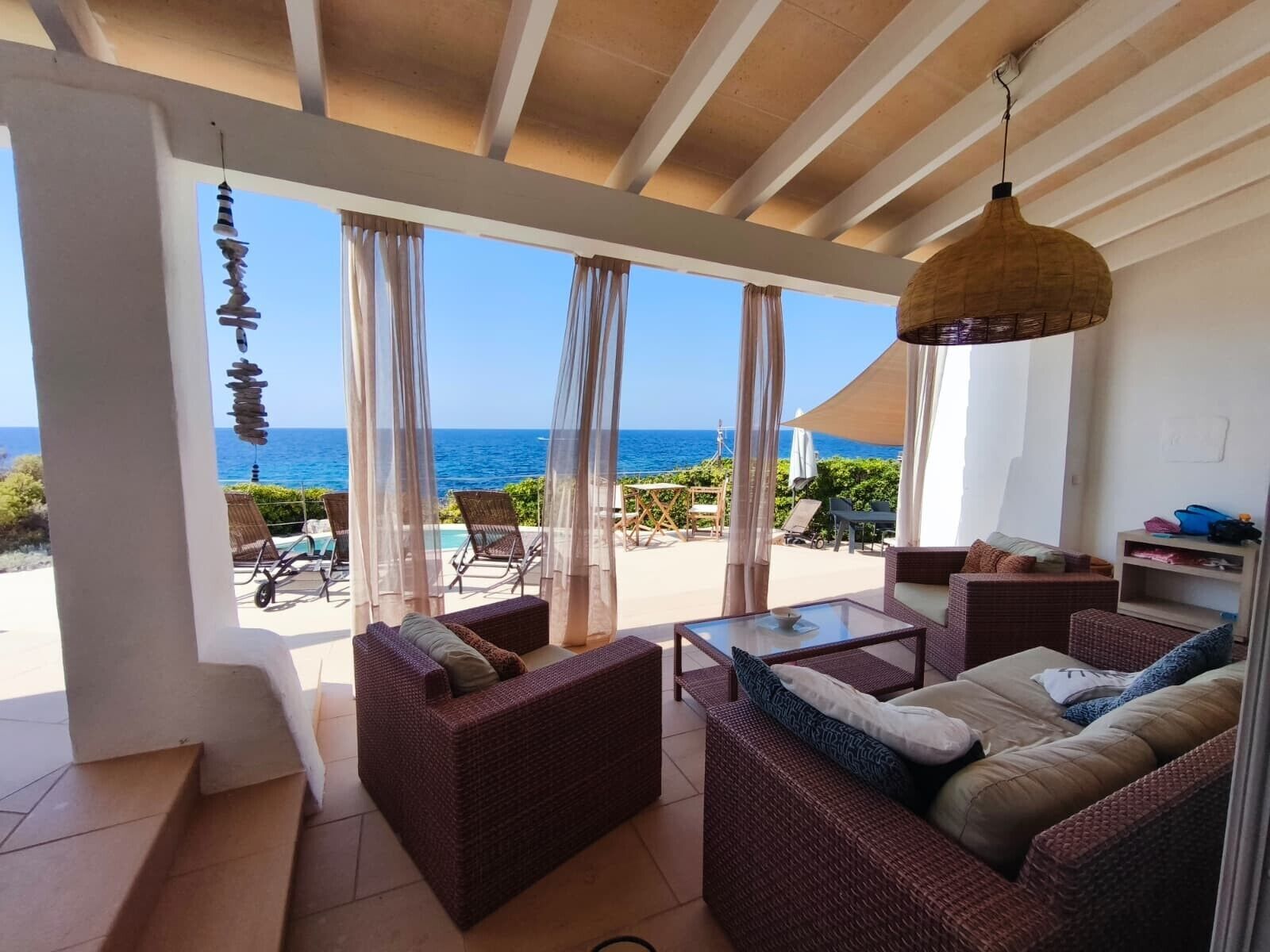 Una habitación con muebles de mimbre, una mesa de vidrio y vista al océano.