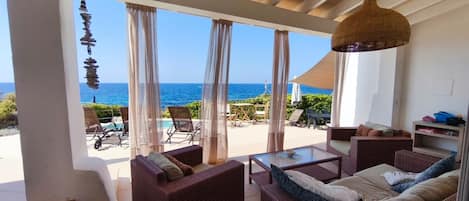 Una habitación con muebles de mimbre, una mesa de vidrio y vista al océano.