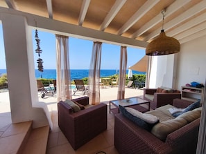 A room with wicker furniture, a glass table, and a view of the ocean.