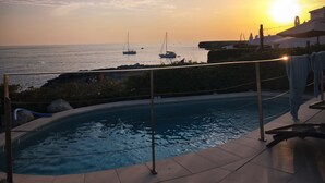 Une piscine avec vue sur la mer et les bateaux, au coucher du soleil.
