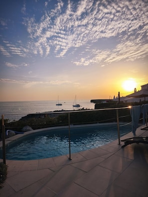 A swimming pool with a view of the sea and boats during sunset.