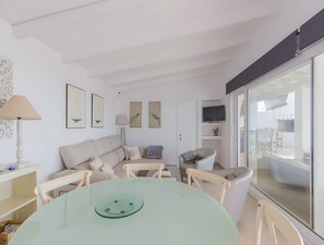 Ein modernes Wohnzimmer mit Glastisch, weißen Möbeln und Bildern an den Wänden.