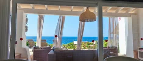 A room with a view of the sea, a wicker sofa, and a hanging light fixture.