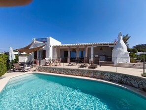 Zona junto a la piscina con una piscina azul cristalina, sillas de descanso y un edificio blanco con balcón.