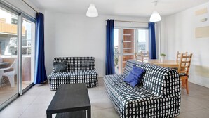A modern living room with a sofa, a coffee table, and a dining area with chairs and a table.