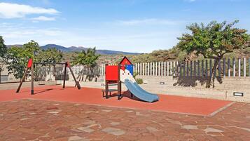 Un'area giochi con uno scivolo, altalene e un recinto.