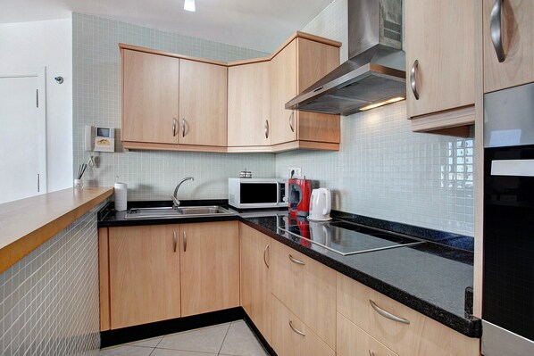 A kitchen with wooden cabinets, a black countertop, a microwave, and a stove.