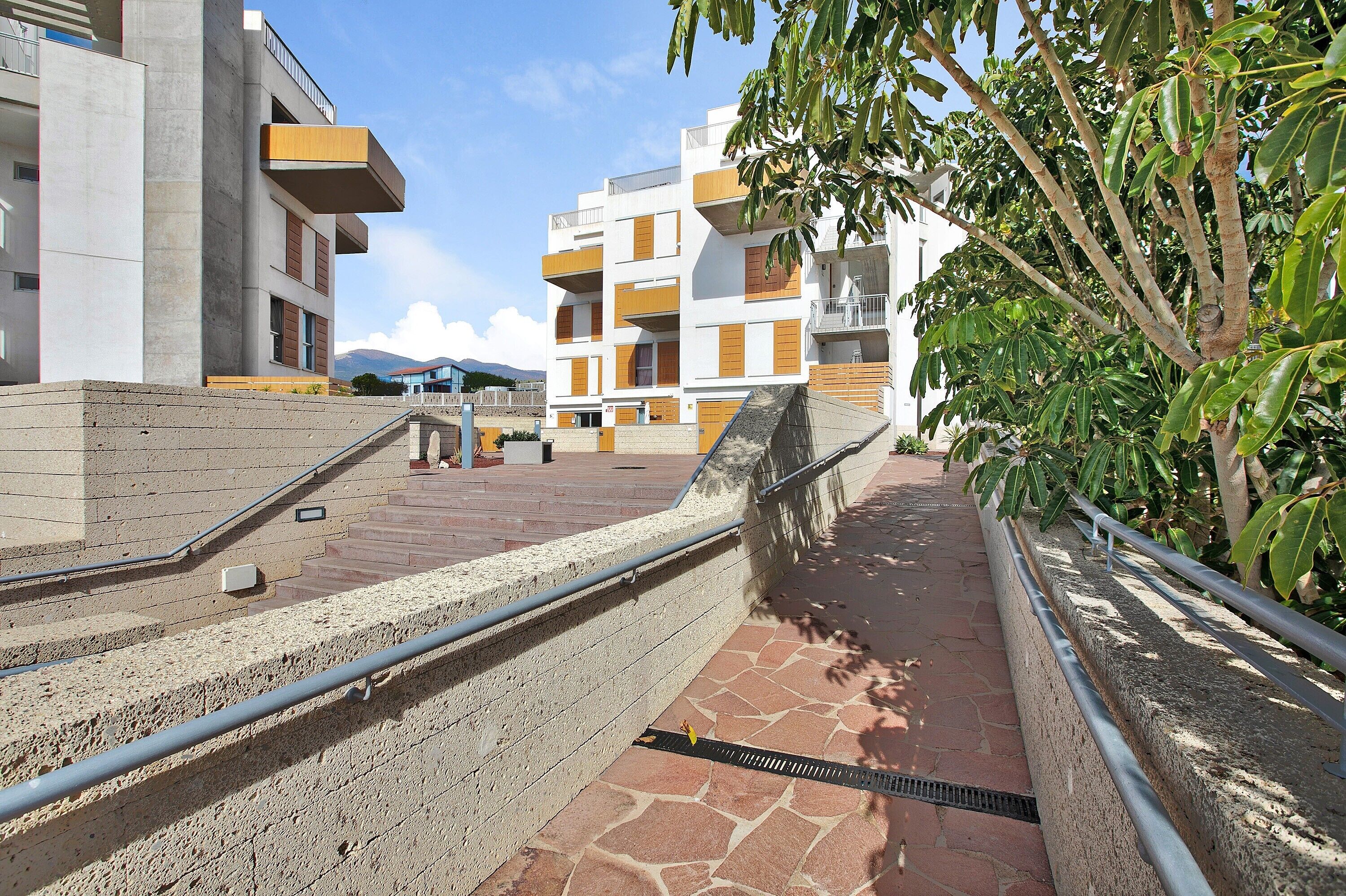 Un edificio moderno con balcones, un sendero de piedra y una barandilla de metal.