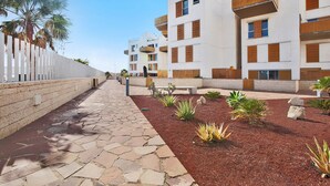 A modern building with multiple balconies, a paved walkway, and landscaped garden beds.