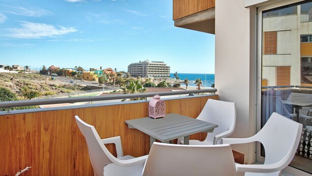 A balcony with a table and chairs, overlooking a beach and buildings.