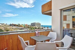 A balcony with a table and chairs, overlooking a beach and buildings.