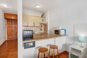 Cocina pequeña con armarios de madera, microondas integrado, cafetera y dos taburetes.