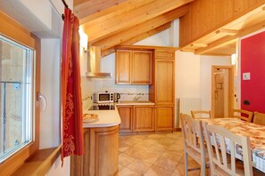 Una cocina con armarios de madera, microondas y comedor con mesa y sillas.