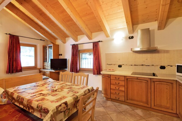 Una habitación con cama, escritorio, televisor y una cocina que incluye armarios de madera y un salpicadero de azulejos.