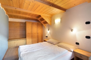 A bedroom with a wooden ceiling, a bed with white bedding, a wooden wardrobe, and wall-mounted lights.