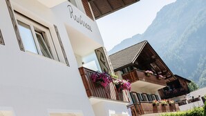 Un edificio con un letrero que dice 'Racine', balcones con barandillas de madera y un paisaje montañoso al fondo.