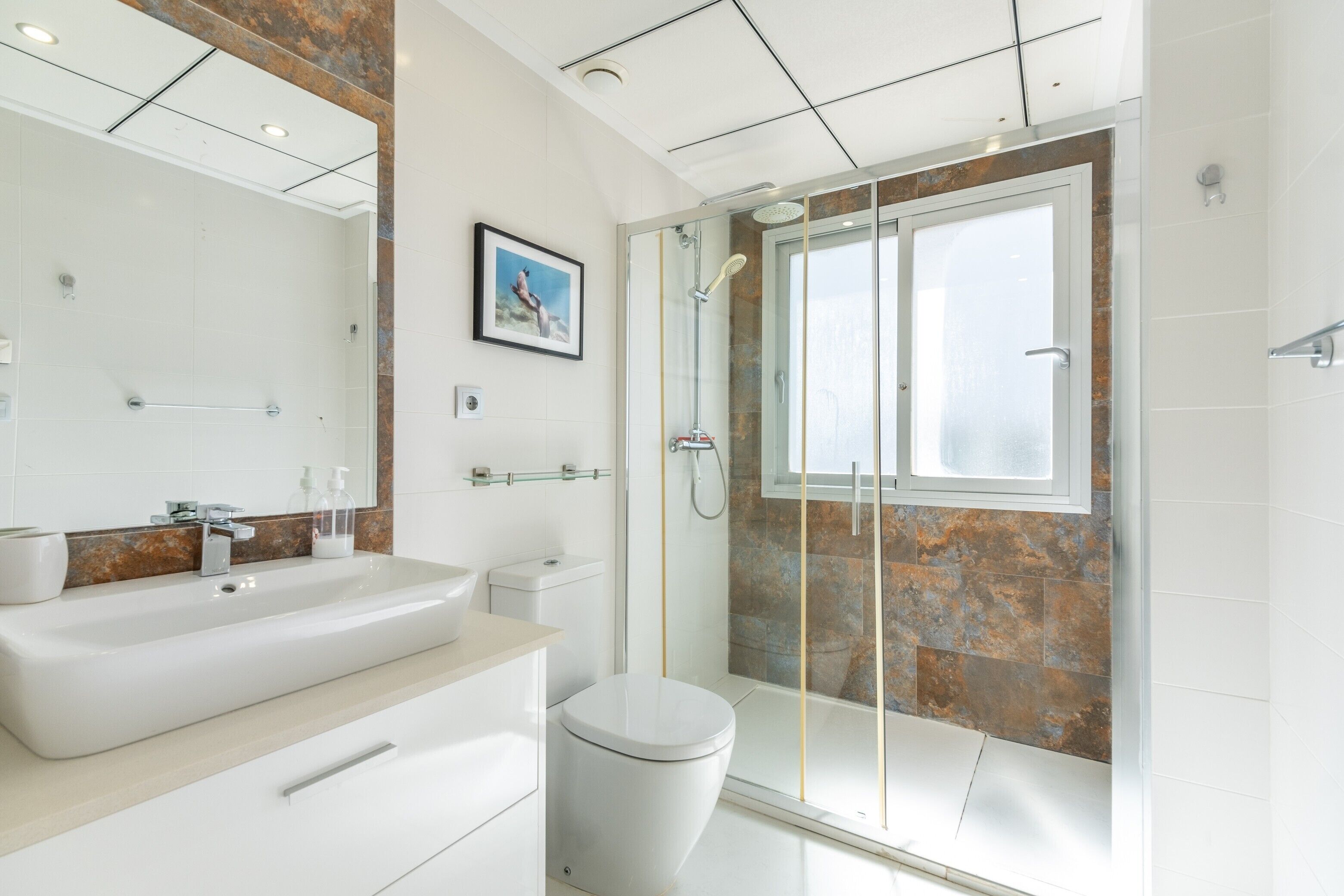 Un baño moderno con una bañera grande, un inodoro y una zona de ducha con mampara de vidrio.