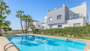 Un espace piscine moderne avec une piscine à l’eau d’un bleu limpide, un escalier de piscine en métal et un bâtiment blanc doté de balcons.