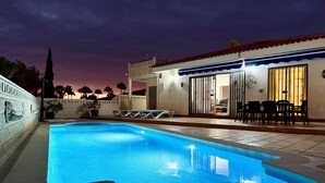 A swimming pool with a tiled deck, a covered patio area with outdoor seating, and a building with a tiled exterior. - Pet Friendly Villa Azul close to the Beach with Pool, Garden, A/C and Wi-Fi (Callao Salvaje, Tenerife)