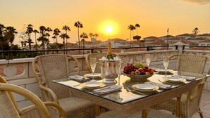 A dining table set for four with wicker chairs, a fruit bowl, and a bottle of champagne. - Pet Friendly Villa Azul close to the Beach with Pool, Garden, A/C and Wi-Fi (Callao Salvaje, Tenerife)