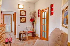 A hallway with a wooden door, a small table with a chair, a vase with red flowers, and a framed picture on the wall.