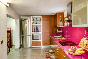 A compact kitchen with a stainless steel refrigerator, wooden cabinets, a pink countertop, and a dining area with a table and chairs.