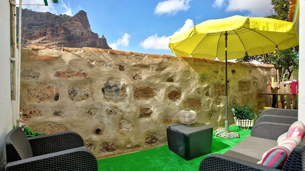 A patio with wicker furniture, a yellow umbrella, and a stone wall. - Holiday Home "Casa del Callejón" with Mountain View, Terrace & Outdoor Shower (Tejeda)