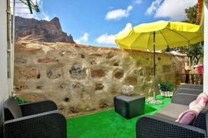 Une terrasse avec des meubles en osier, un parasol jaune et un mur en pierre.