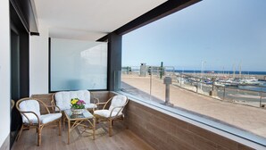 Un balcon agrémenté de meubles en osier et d’une table en verre, offrant une vue sur une marina avec des bateaux et un ciel dégagé.