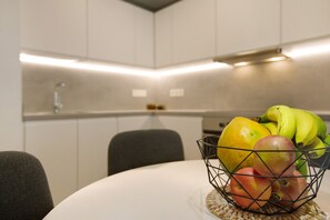 Une cuisine avec des armoires blanches, un plan de travail blanc et un panier de fruits sur la table.