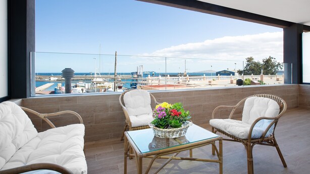 Un balcon agrémenté de meubles en osier, d’une table en verre et d’une plante en pot.