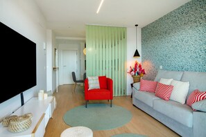 Un salon doté d’un téléviseur à écran plat, d’un fauteuil rouge, d’un canapé gris avec des coussins à rayures et d’un mur vert à motifs.