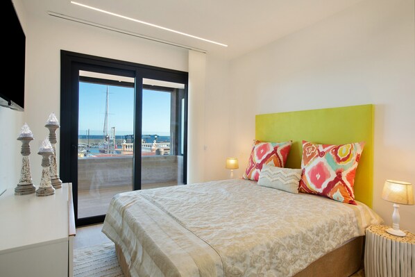 Une chambre à coucher avec un lit, une table de chevet, une lampe et une vue sur l’extérieur, accessible par une porte coulissante.