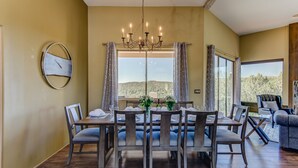 A dining area with a chandelier, a round wall clock, and a view of the outdoors. - Sedona Blue Jay Close Access To Numerous Trails, Hot Tub, Patio, Walkable (Sedona)