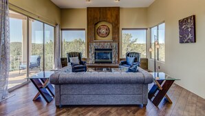 A spacious living room with a fireplace, large windows, and a view of the outdoors. - Sedona Blue Jay Close Access To Numerous Trails, Hot Tub, Patio, Walkable (Sedona)
