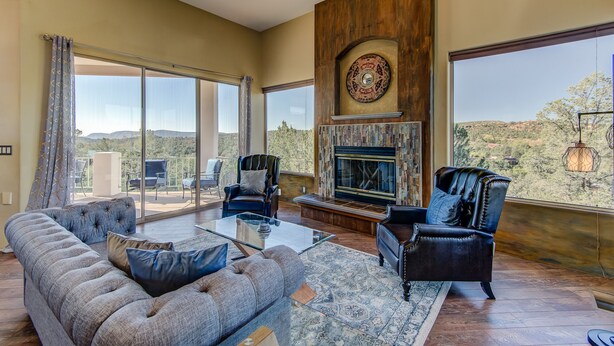 A spacious living room with a fireplace, large windows, and a balcony with outdoor seating. - Sedona Blue Jay Close Access To Numerous Trails, Hot Tub, Patio, Walkable (Sedona)