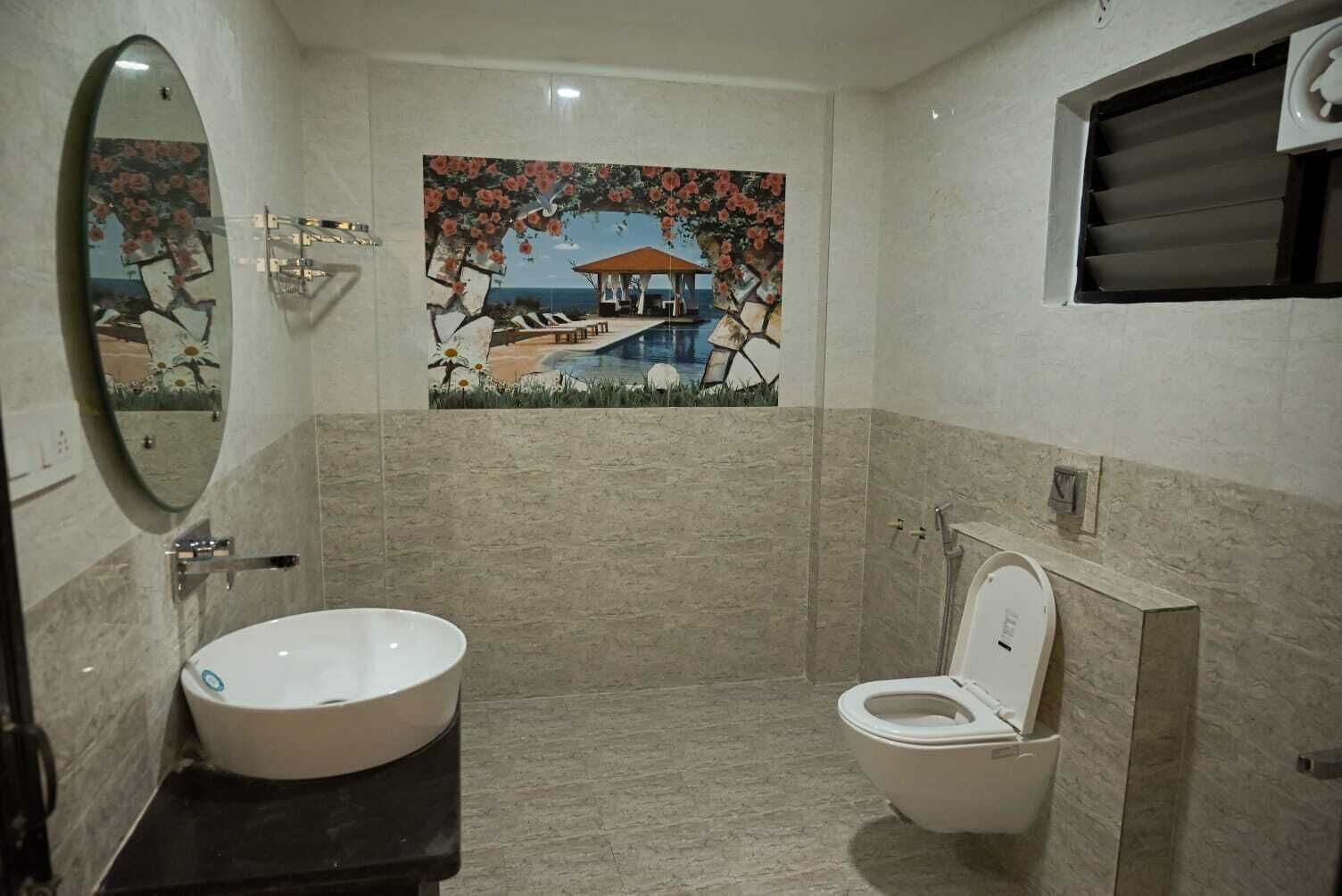 A bathroom with a large oval mirror, a sink, a toilet, and a decorative wall mural depicting a beach scene.