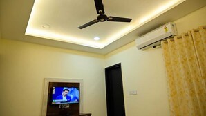 A room with a ceiling fan, an air conditioning unit, a television, and a door. - Hotel Golden Bliss (Bhopal)