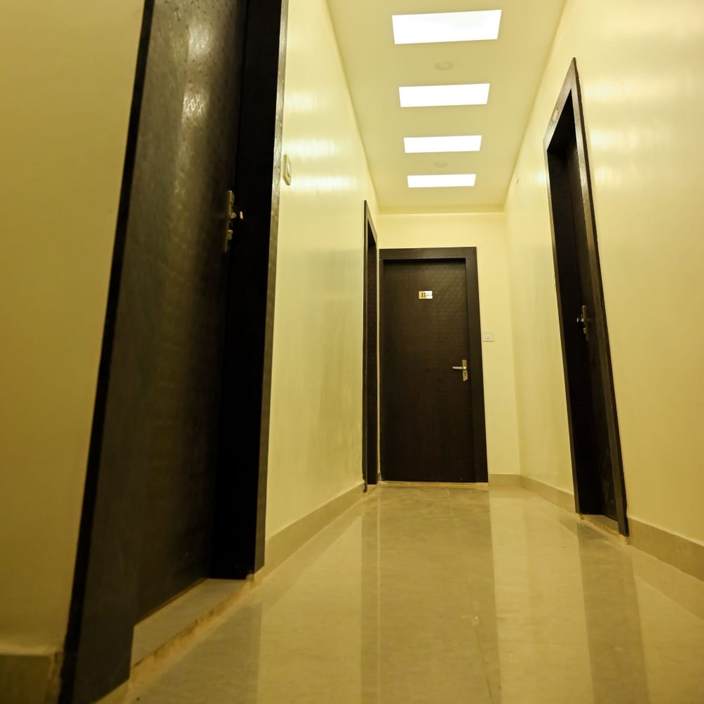 A hallway with a dark door at the end, a light fixture on the ceiling, and a tiled floor.