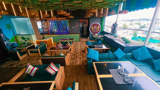 A modern restaurant with green seating, wooden tables, and a view of the city. - Hotel Golden Bliss (Bhopal)