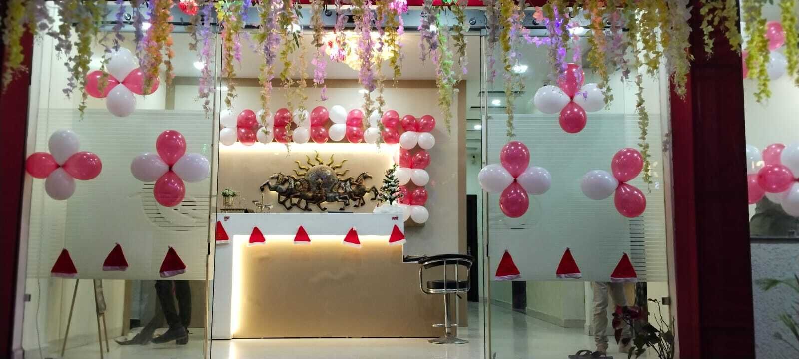 Zona de recepción con un mostrador, pared decorativa con motivos de sol, y arreglos florales colgantes.
