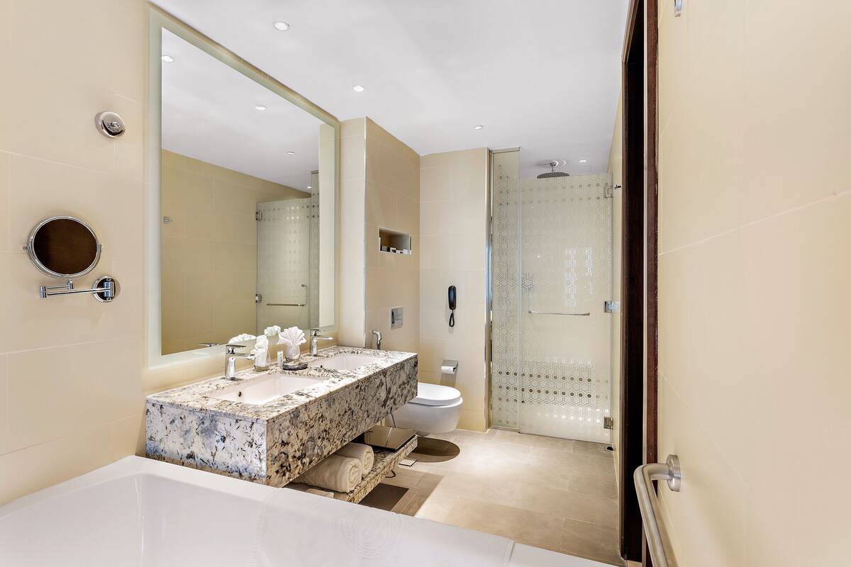 A modern bathroom with a large mirror, a marble sink, a toilet, and a shower area.