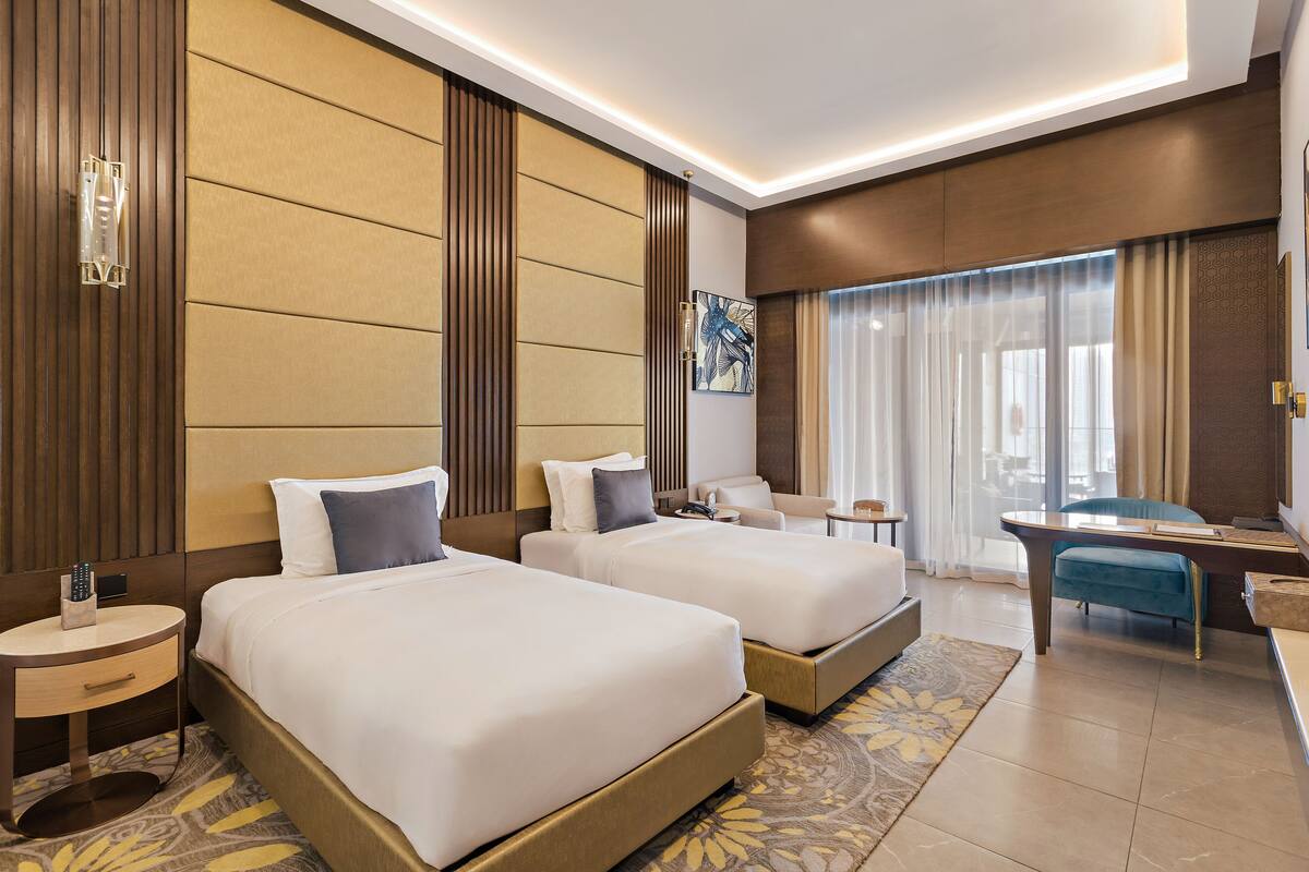 A hotel room with two beds, a desk, a chair, a small table, and a window with curtains.