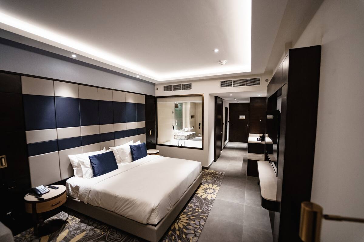 A modern hotel room with a large bed, bedside tables, a mirror, and a view of the bathroom.