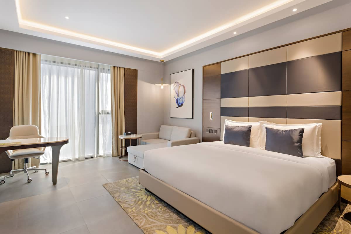 A modern hotel room with a large bed, a desk, and a sofa.