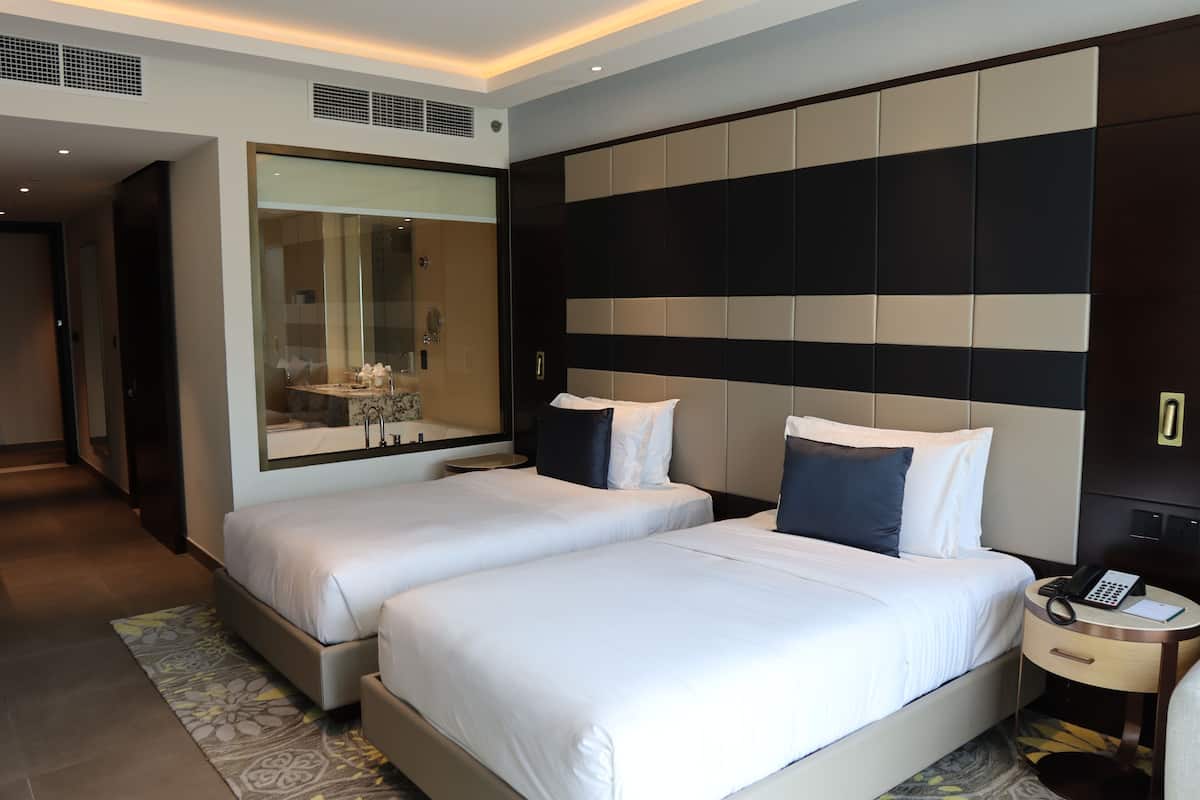 A hotel room with two beds, a large mirror, a bedside table with a phone, and a modern design.