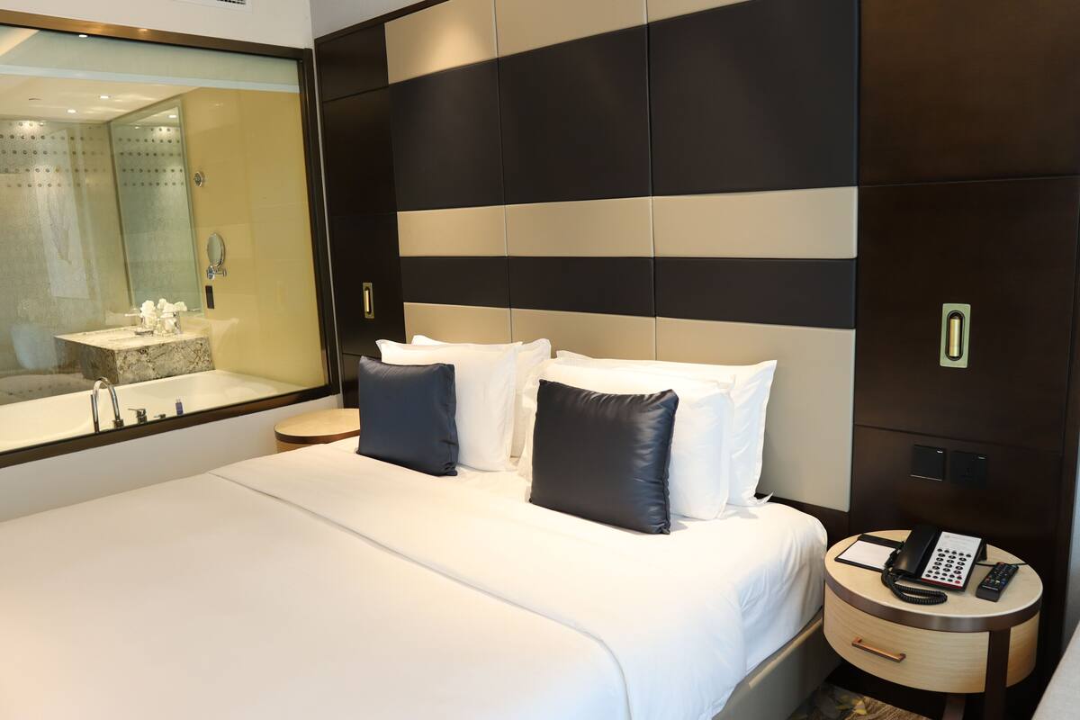 A hotel room with a large bed, a bedside table with a phone and a notepad, a mirror, and a view of the bathroom.