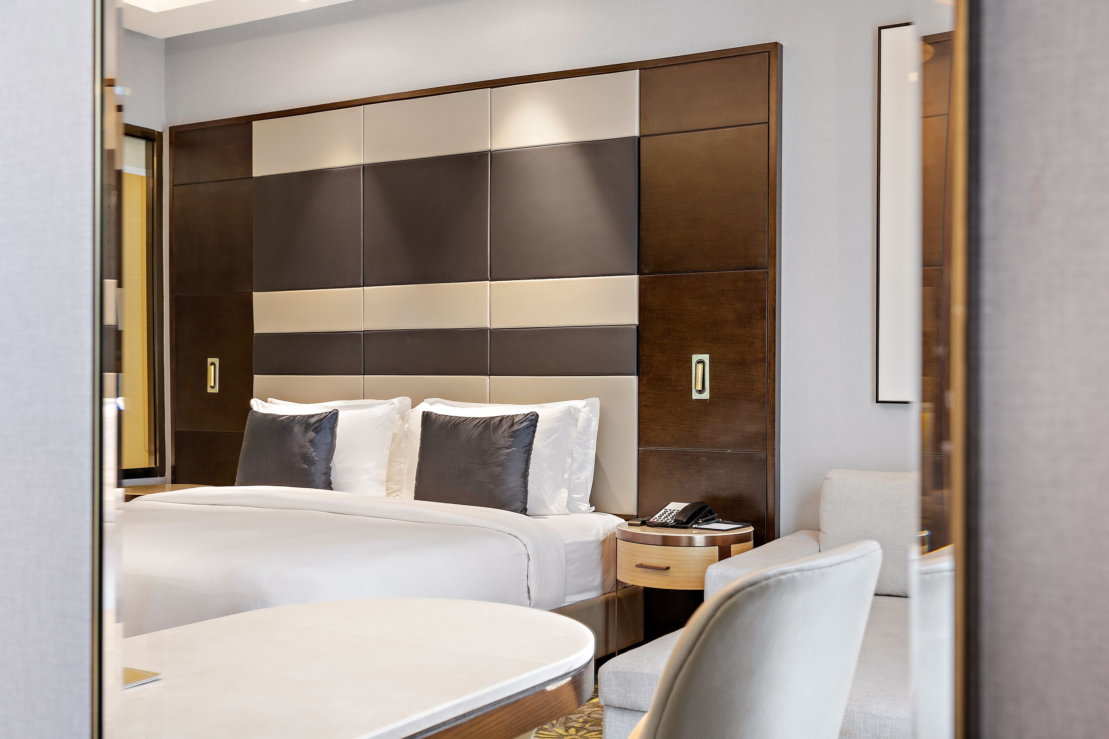 A hotel room with a large bed, a bedside table with a phone, a chair, and a wardrobe with a modern design.